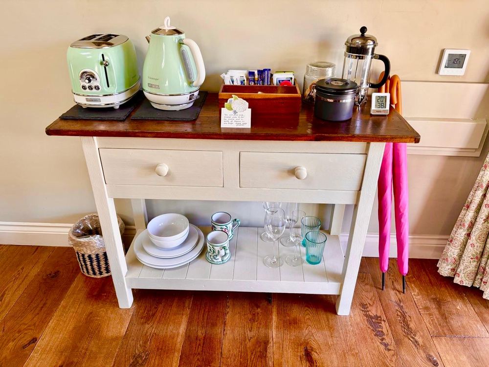 A painted tea station with a sage kettle and toaster, cafetière, mugs and glasses